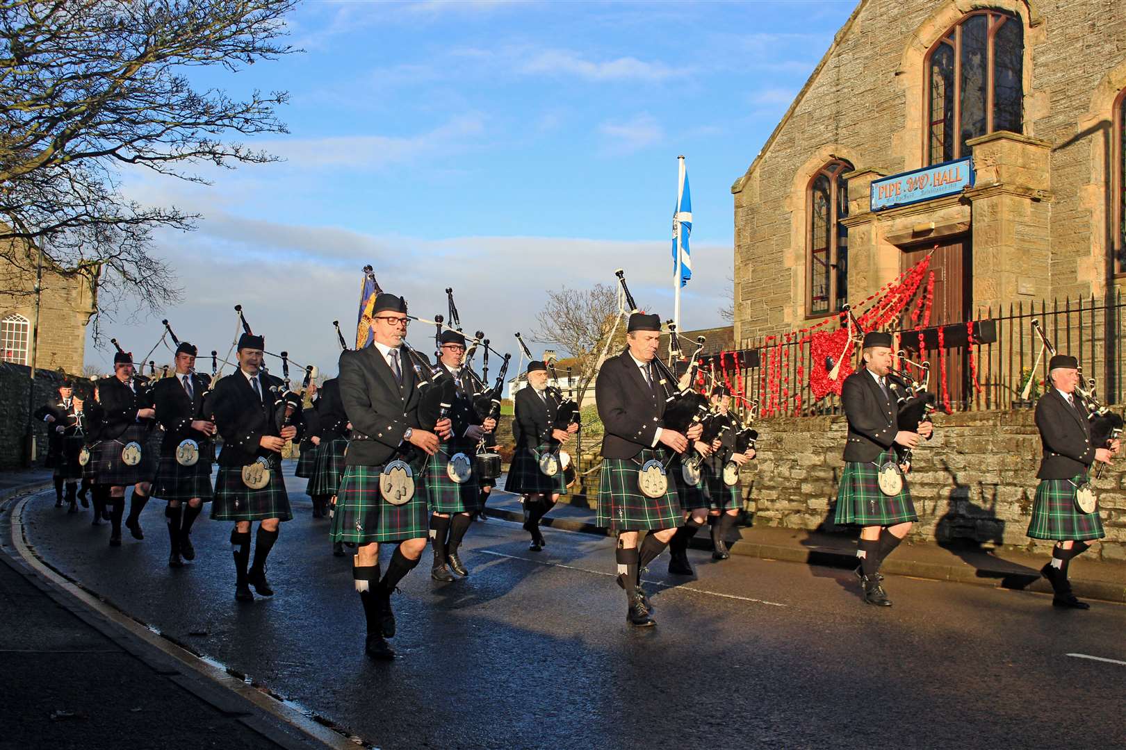 Members of Wick RBLS Pipe Band marching past the Pipe Band Hall on their way to the war memorial for the 2023 Remembrance Sunday parade. The railings outside the hall had been decorated with poppies by Caithness Community Connections. Picture: Alan Hendry