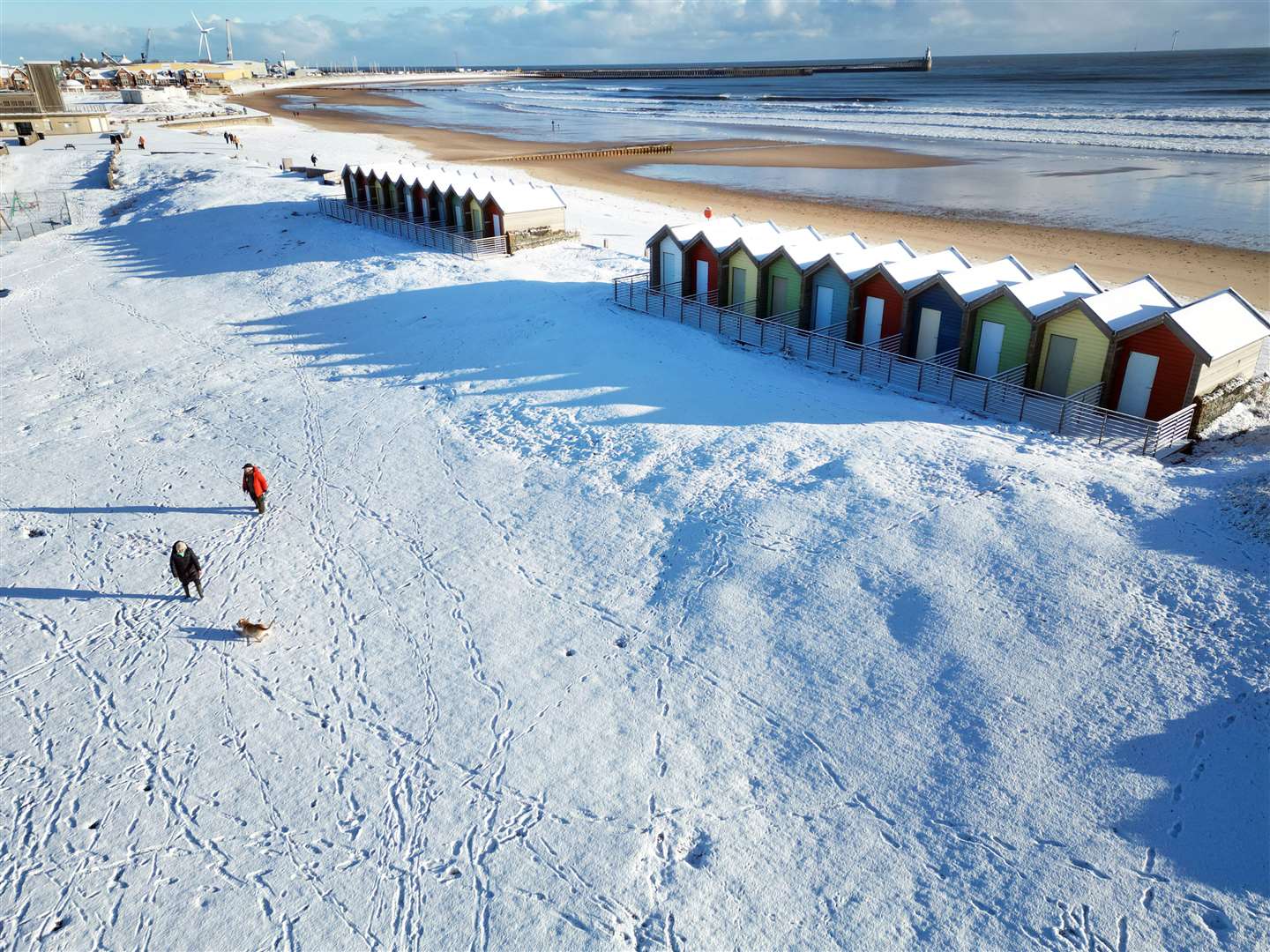 People walk their dogs through the snow beside the beach huts at Blyth in Northumberland (Owen Humphreys/PA)