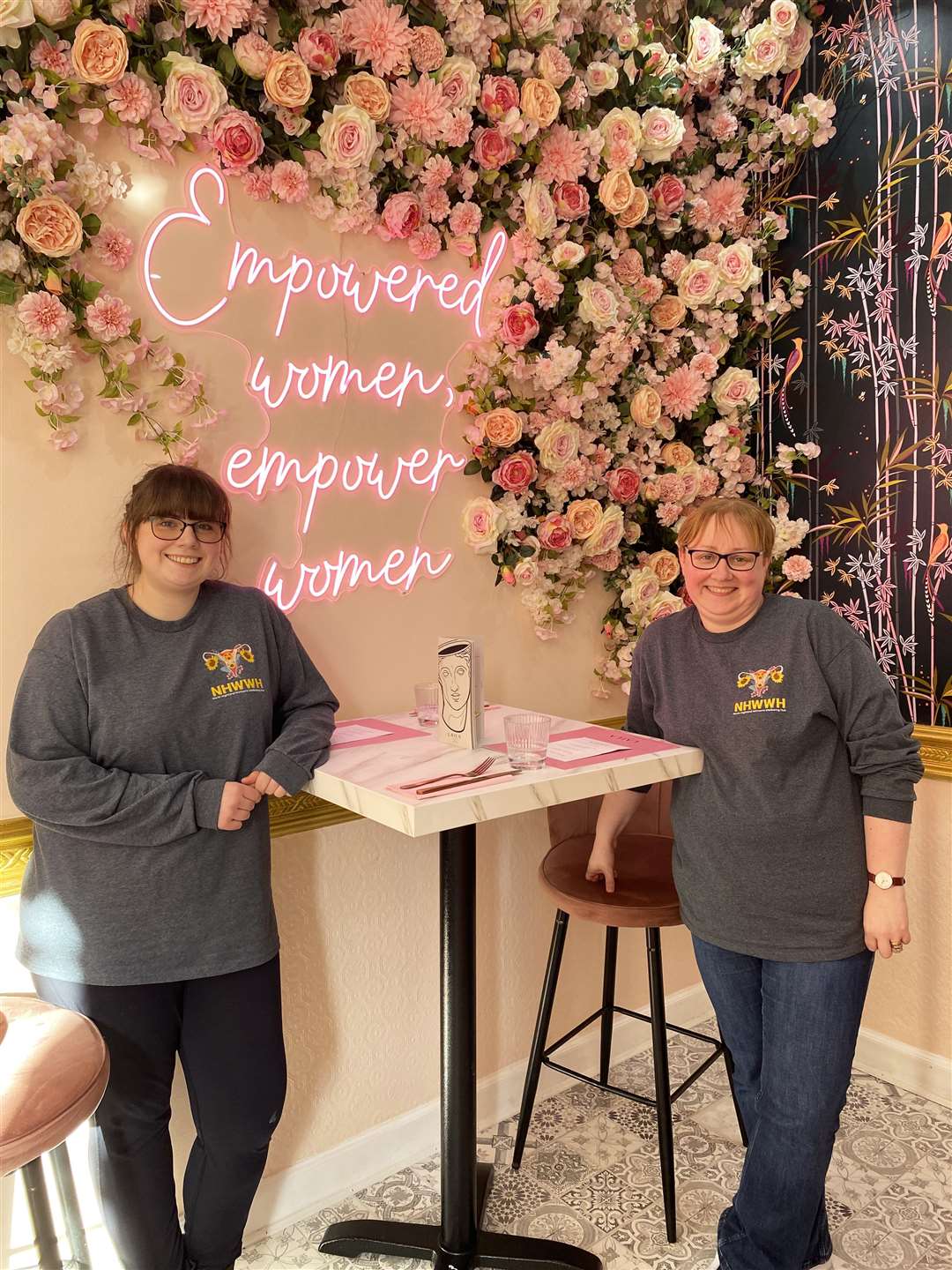 Rebecca Wymer and Kirsteen Campbell of North Highland Women’s Wellbeing Hub beside a women's empowerment message at Laila bistro in Edinburgh.