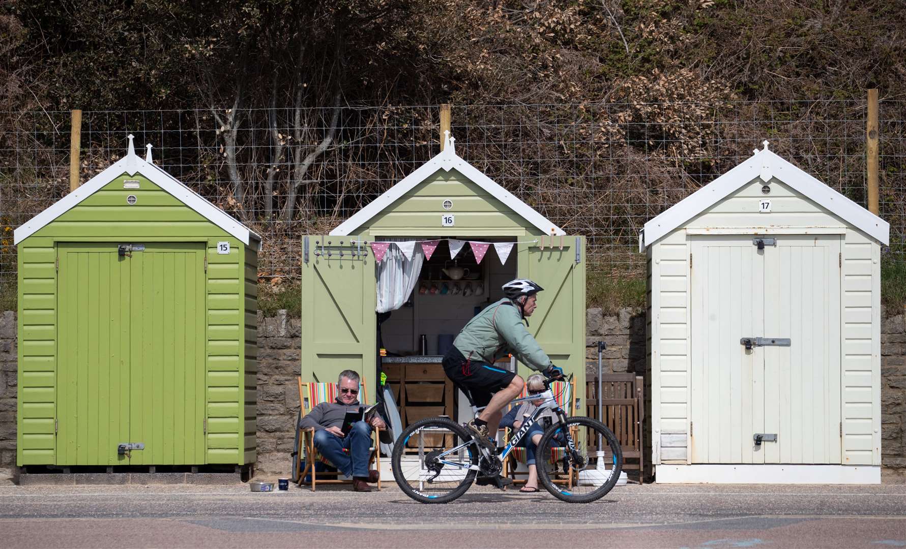 A cyclist passes people enjoying the warm weather outside their beach hut on Bournemouth beach (Andrew Matthews/PA)