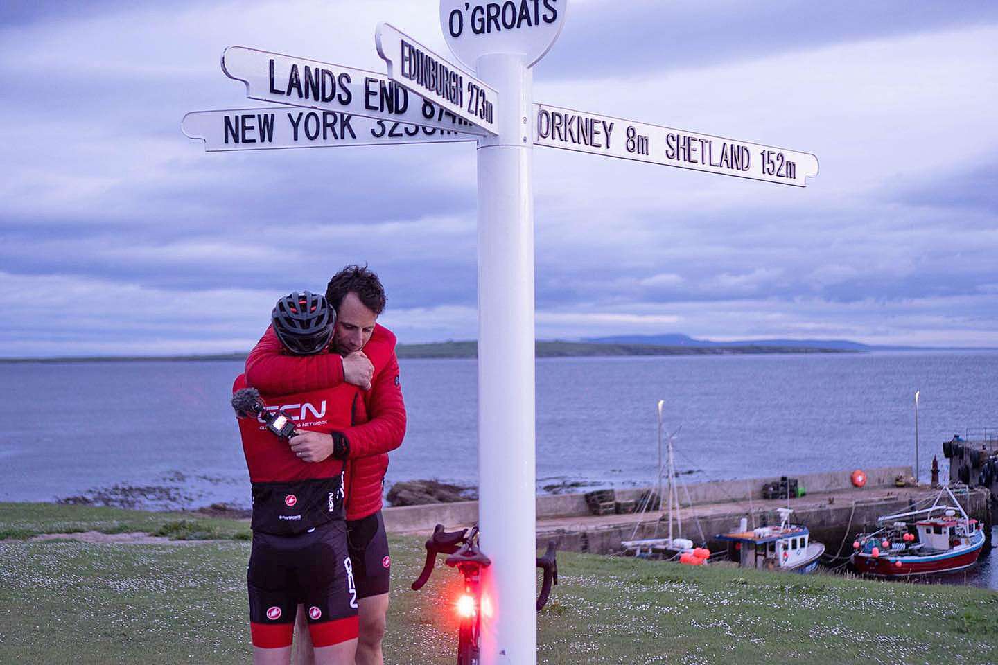 Mark Beaumont and James Lowsley Williams embrace under the signpost at John O'Groats at the end of their epic journey from Land's End.