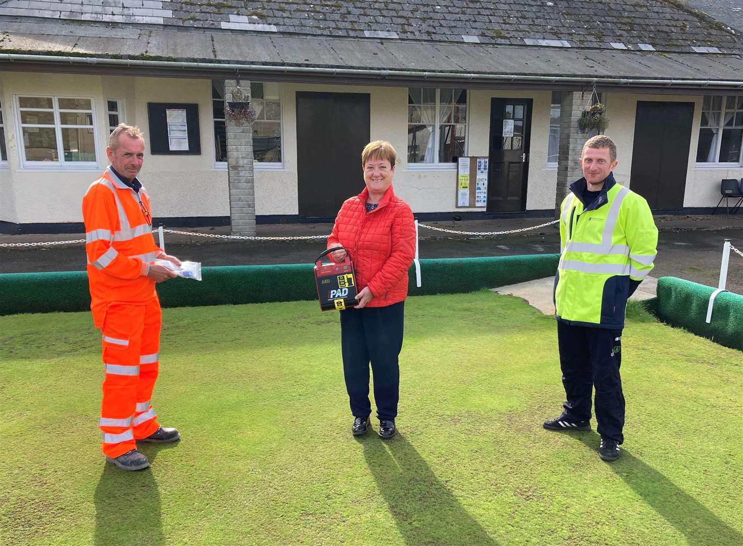 BAM site foreman Paul McQuade (left) and Andrew Henderson (right), SSEN Transmission construction manager, presenting the defibrillator to Sharon Rosie, a member of the Rosebank Bowling Club, who accepted it on behalf of all at Rosebank/Wick Youth Hub.
