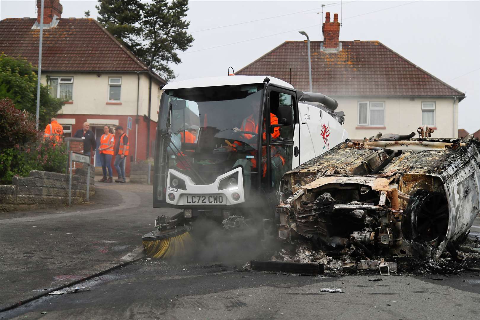 Council workers clear debris from the area immediately around a car that was set alight during the riot (PA)